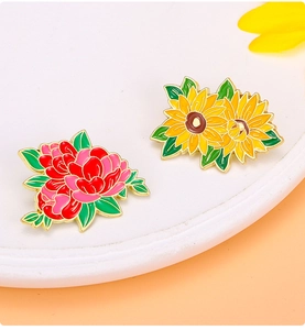 Detailed close-up of colorful enamel peony and sunflower metal brooch pins on a tray