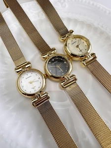 Close-up of three vintage gold quartz watches with mesh straps on a white relief plate