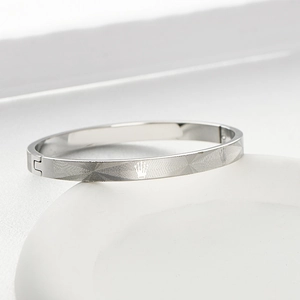 Detailed view of silver stainless steel bangle with crown motif and radial grid texture