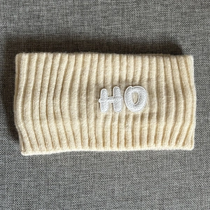 Macro detail of ribbed knit headband in cream with textured HO letter patch