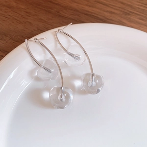 Detailed view of elegant silver cherry earrings with clear heart glass charms on a white plate