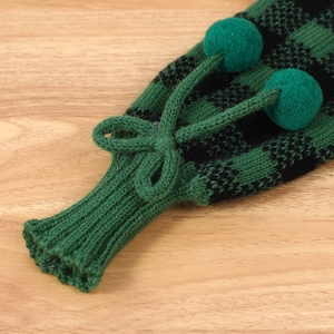Détail macro du cache-bouteille tricoté à carreaux verts avec pompon et nœud décoratif