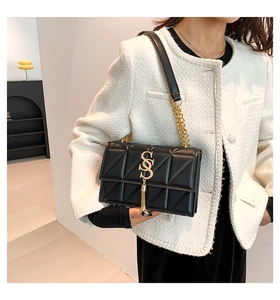 Detail of black quilted shoulder bag featuring gold SS logo, tassel, and chain strap