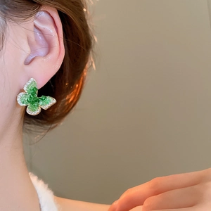 Detailed view of emerald butterfly earrings with 18k gold plating on model's ear
