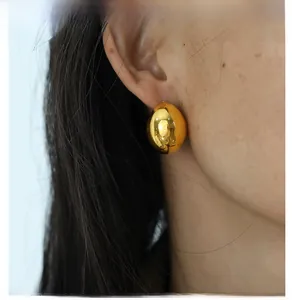 Close-up of a high-polish gold teardrop earring worn by a model in a minimalist style