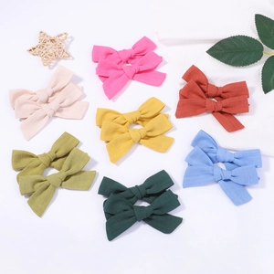 Flat lay of colorful linen bow hair clips with soft fabric texture in seven bright colors