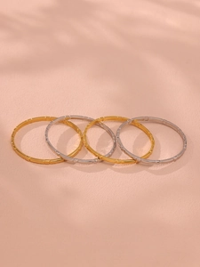 Macro shot of tiered gold and silver bangles with bamboo texture on a soft peach surface