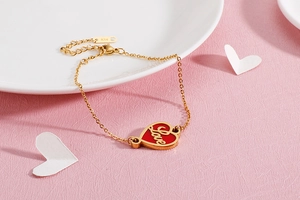 Close-up of gold chain bracelet with red enamel heart pendant and Love engraving