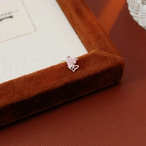 Macro shot of silver heart and butterfly stud earrings with pink gemstone on a velvet stand
