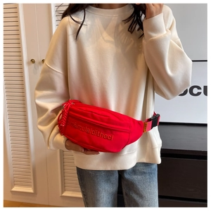Detail of red canvas waist bag with embroidered text and colorful striped crossbody strap