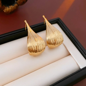 Macro detail of gold-plated leaf earrings with vertical striped texture on white padding