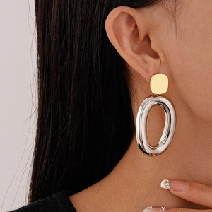 Macro shot of gold square and silver oval geometric earrings worn by a model
