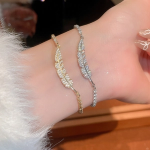 Close-up of zircon-studded feather bracelets in gold and silver on a model wrist
