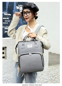 Close-up of stylish grey diaper backpack with slogan label held by a casual female model