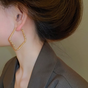 Model wearing large irregular gold geometric diamond earrings with a textured surface