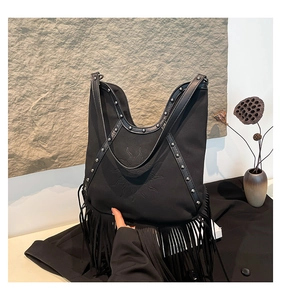 Detail of bohemian black tote bag featuring sun face embroidery, rivets and long fringe