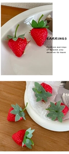 Detail of red strawberry hair clip with golden metal base on a white ceramic plate