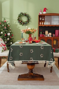 Close-up of green Christmas tablecloth with berry wreath patterns and beige tassels