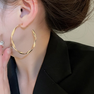 Polished gold-plated twisted hoop earring worn by model to show size and metallic texture
