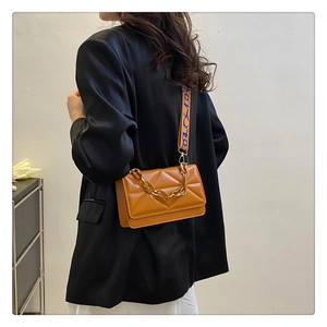 Detail of caramel brown quilted small square bag with resin chain and wide woven strap