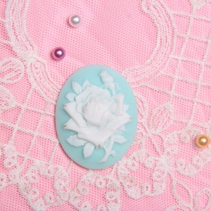 Close-up of vintage light blue oval rose cameo with 3D white floral resin relief detail