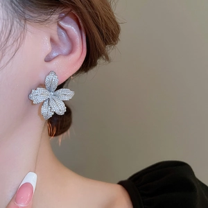 Macro shot of silver flower earrings with pavé crystals on a model's ear