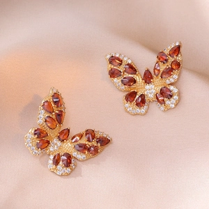 Macro view of butterfly earrings with red gemstones and zircons on champagne silk