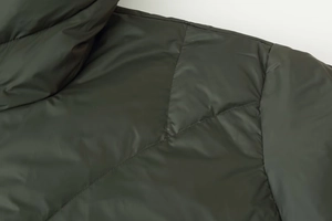 Close-up of high-density stitching and quilted seams on dark green hooded cotton coat