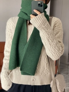 Detailed texture of thick green knitted scarf paired with a beige cable knit cardigan