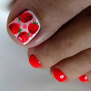 Detail of red press-on toenails featuring a white base with cute strawberry patterns