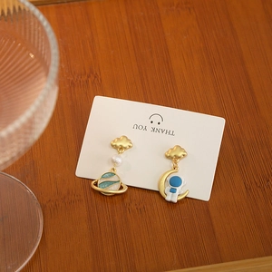 Creative astronaut and planet asymmetric drop earrings on white card and wood background
