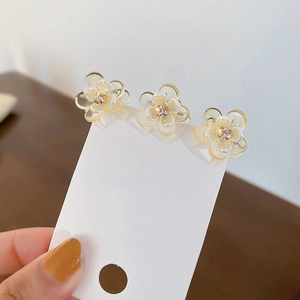 Detail view of three mini flower hair claws with cream white resin petals and diamond centers