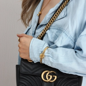 Detail of gold knot open cuff bracelet and mushroom pendant necklace with a quilted bag