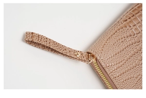 Detalle de cartera color topo con textura de cocodrilo, cremallera dorada y asa de mano
