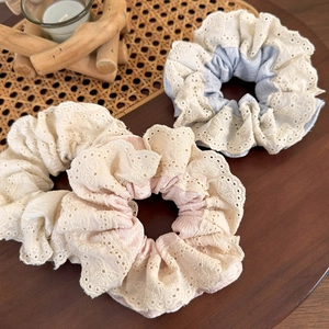 Detailed view of floral lace scrunchies in beige, pink and blue fabric on a rustic tray
