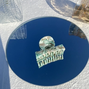 Artistic close-up of marble pattern acetate hair claw clip reflecting on a round mirror