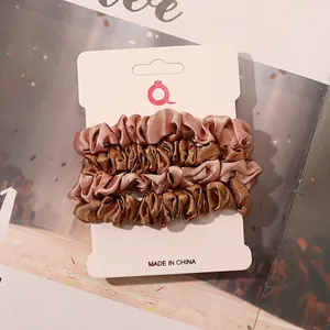 Close-up of four satin scrunchies in rose pink and bronze on display card pack
