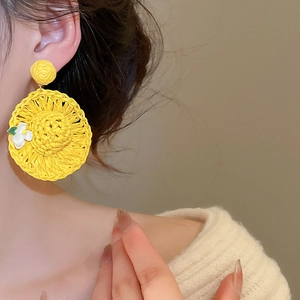 Macro shot of yellow raffia woven earrings in a summer straw hat design on model