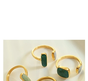 Macro shot of three gold-plated open rings featuring square green and gray gemstones