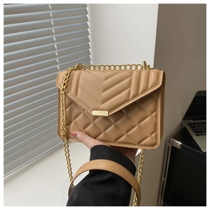 Detail of light brown quilted bag with V-shaped stitching and golden chain strap