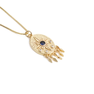 Detail of gold evil eye pendant with blue zircon stone and hanging tassel charms