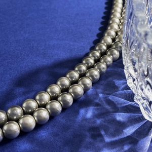 Close-up of elegant champagne pearl necklace on smooth dark blue silk with crystal glass