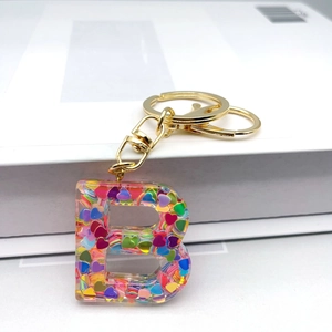 Detailed close-up of resin letter B keychain with colorful heart sequins and gold hardware
