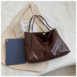 Detailed view of dark brown tote bag made of soft faux leather on cream blazer