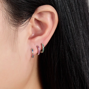 Close-up of elegant small hoop earrings with colorful zircon stones on the ear