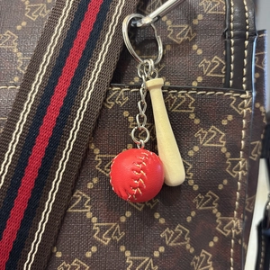 Mini wooden baseball bat and red-stitched ball keychain hanging on a brown handbag