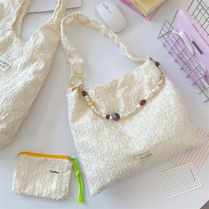 Detail of cream lace tote with floral texture and vintage bead strap accent