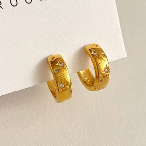 Detail of gold C-shaped hoop earrings featuring engraved stars and sparkling zircon stones