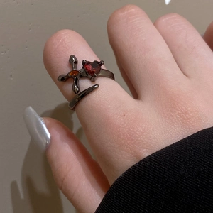 Detail of gothic black open ring featuring a red heart stone and orange cross inlay