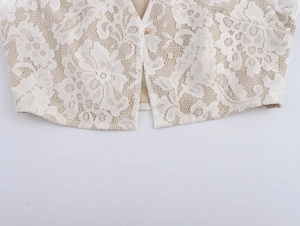 Close-up of white hollow lace fabric texture and detailed metal button on elegant cardigan